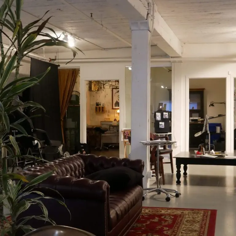 Mesa studio lounge with a leather couch, plants, and stations in the background