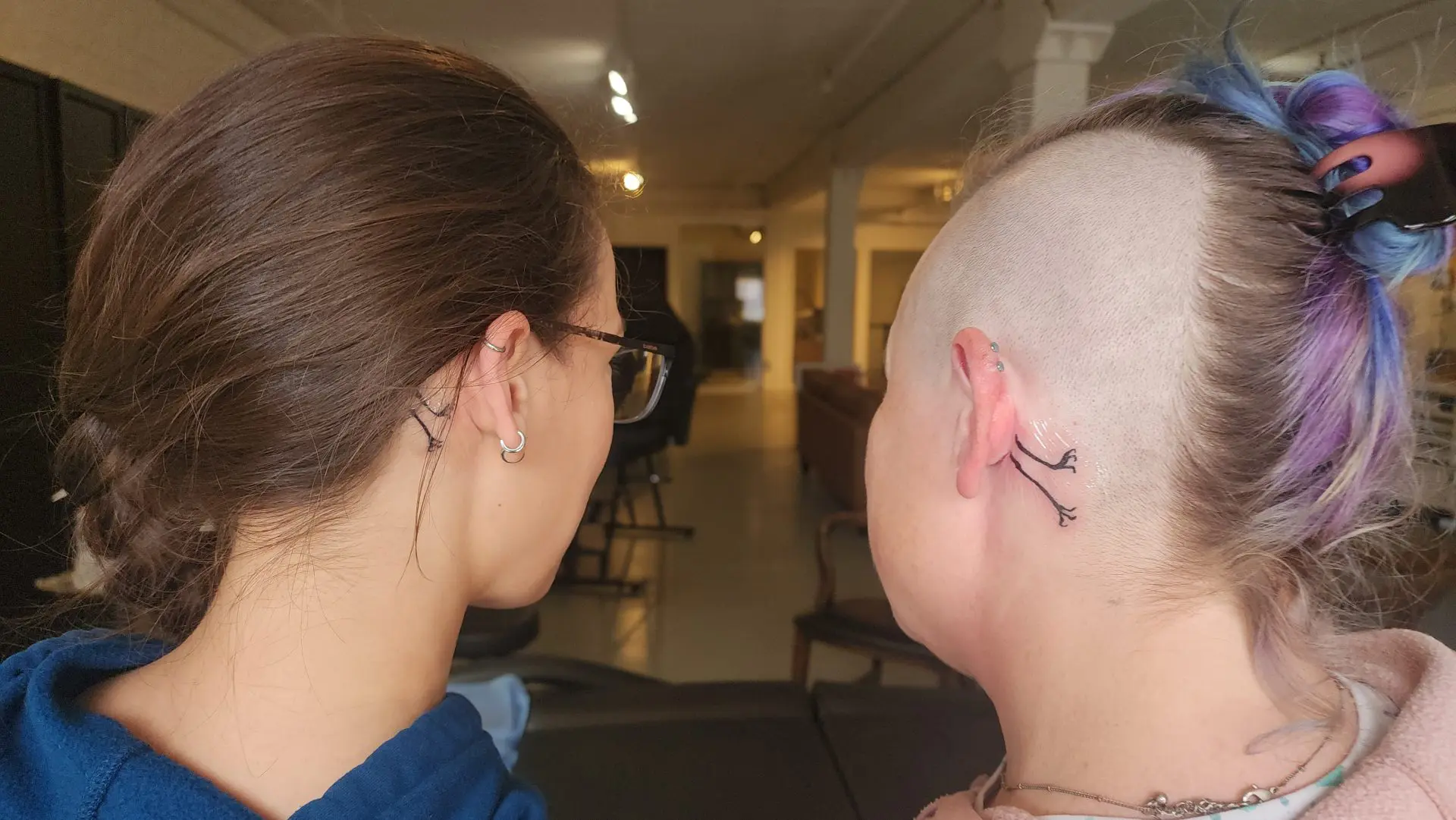 Two friends from behind showing matching racoon leg tattoos from Simkaye's Racoon comic behind their ears