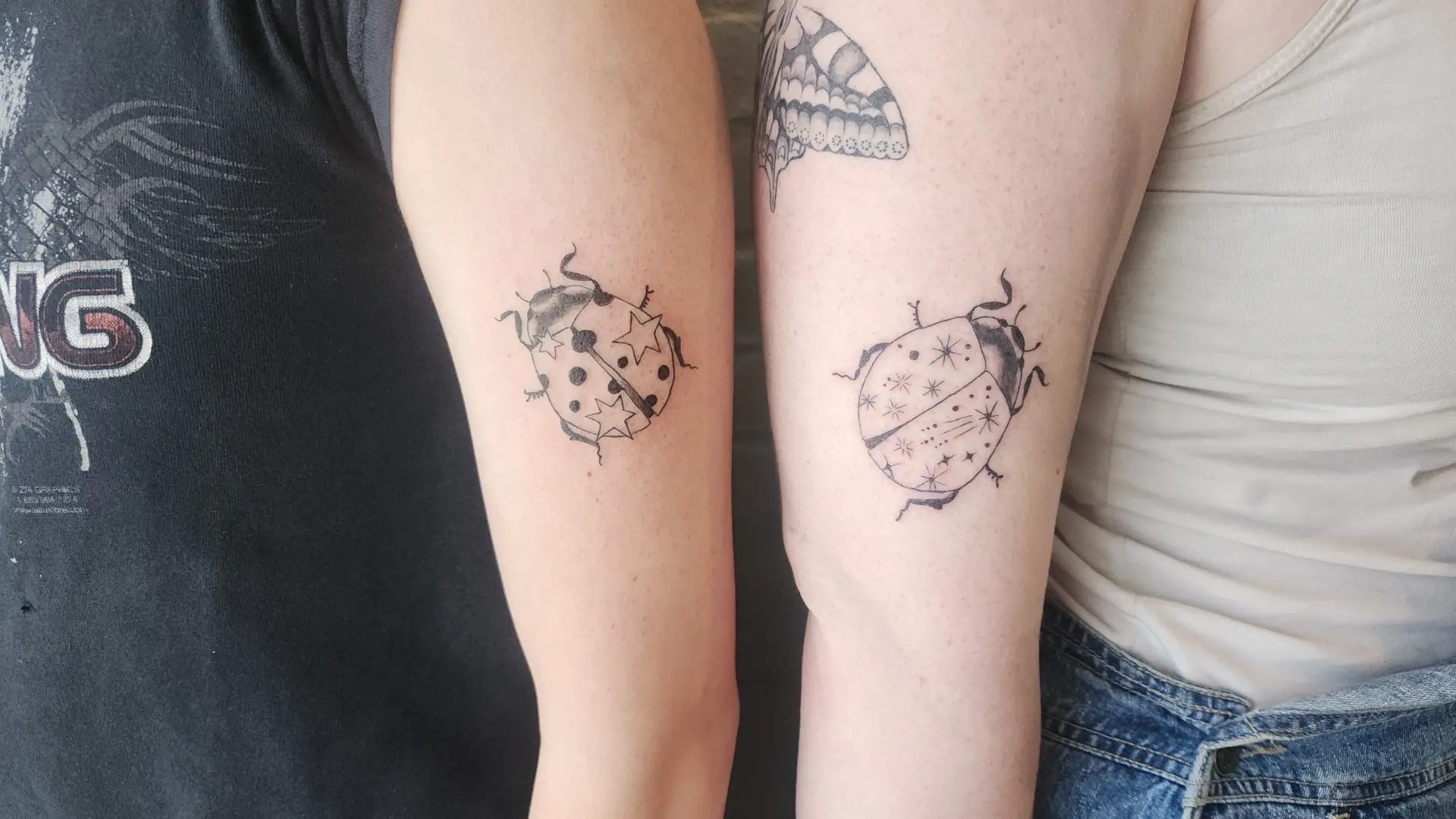 Two matching ladybug tattoos on two people’s arms, one with stars and dots, one with sparkles