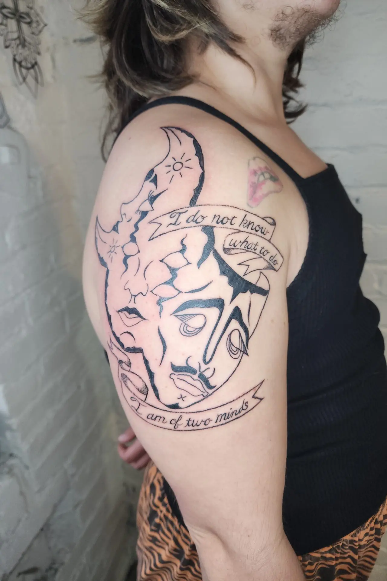 Crescent moon and two faces with banners reading I do not know what to do and I am of two minds, on an upper arm