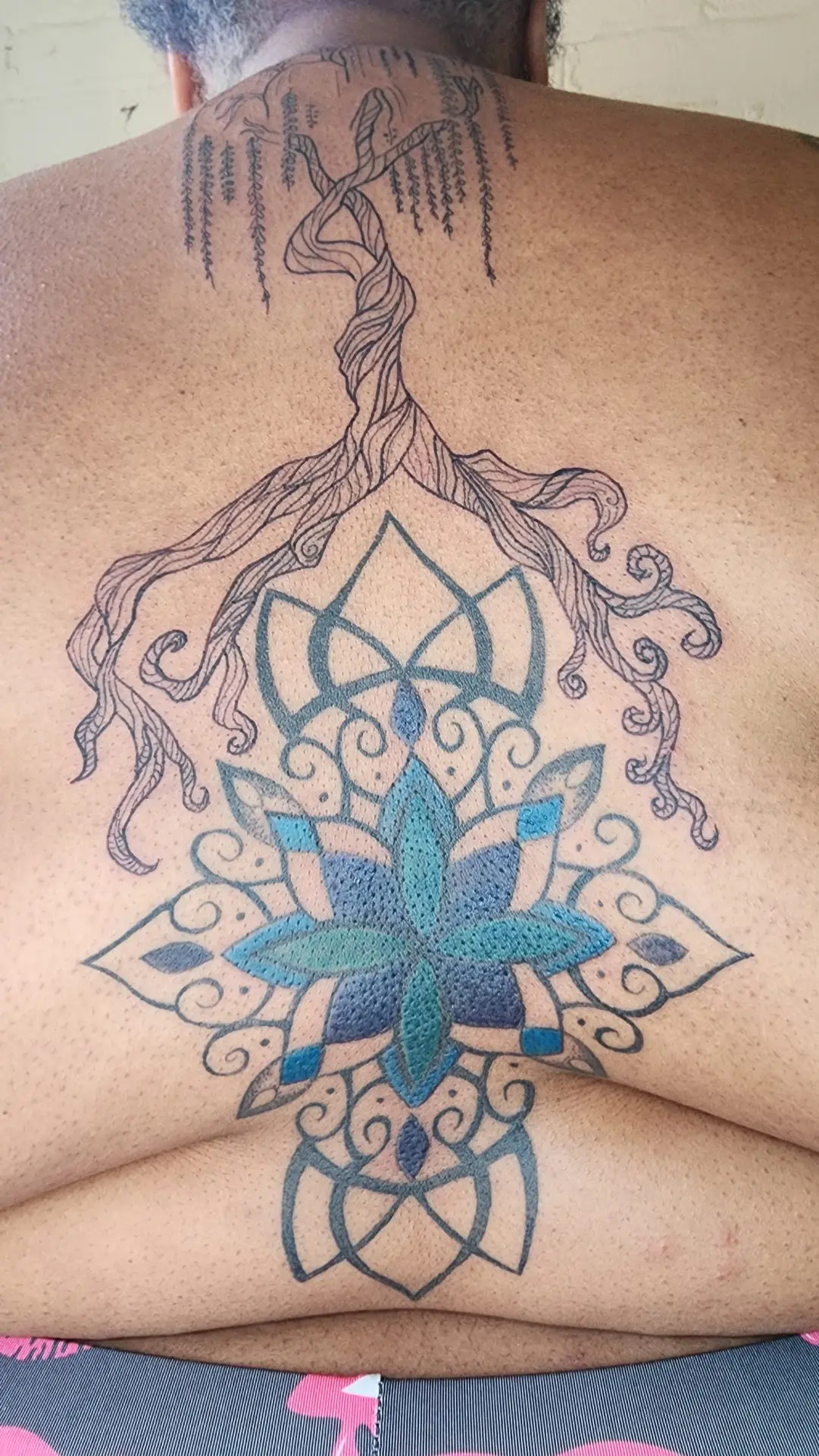 Weeping willow with roots flowing into a blue and teal lotus mandala, running down the center of a back