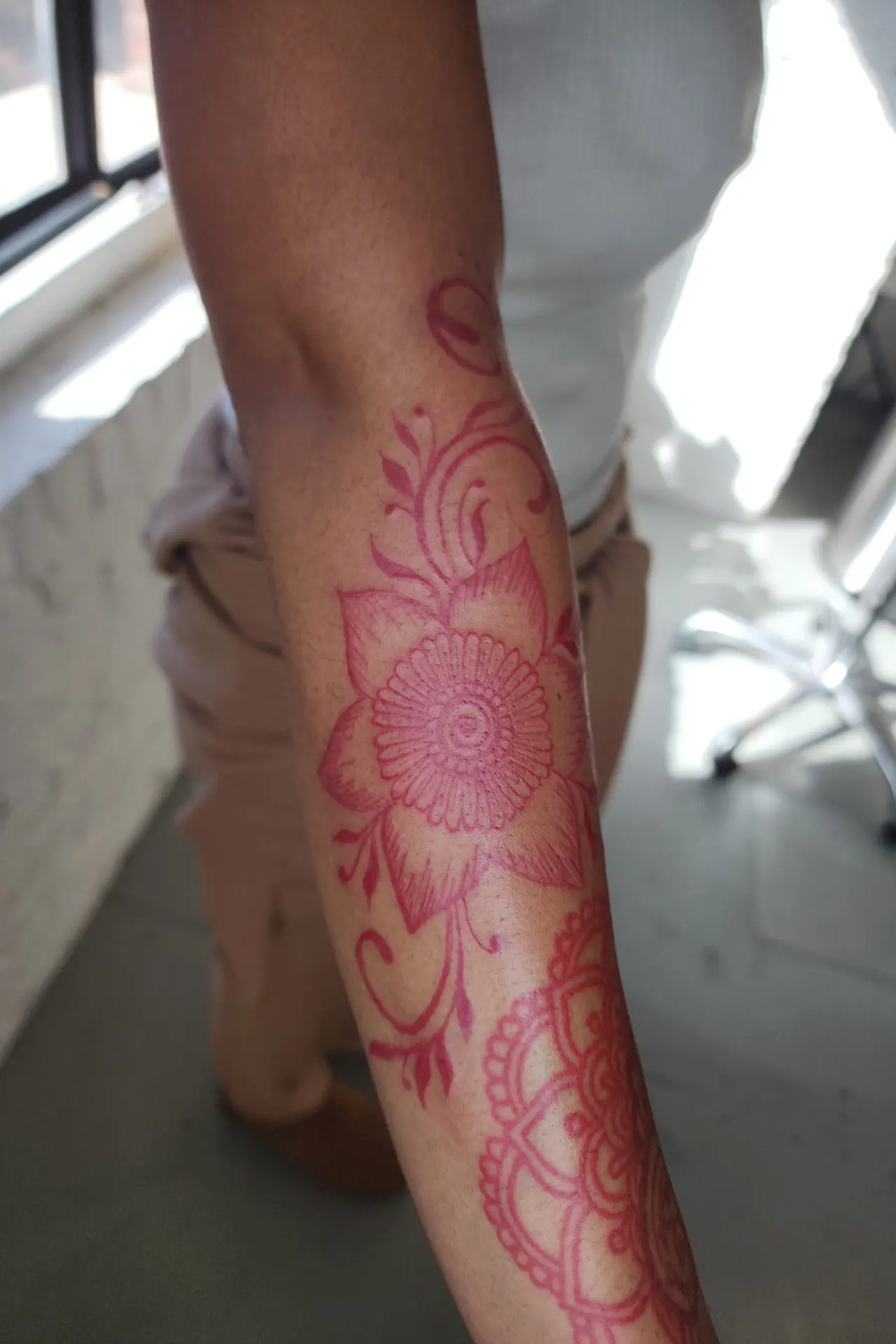 Close-up of a red ink flower with a spiral center and fine-line hatching on a forearm